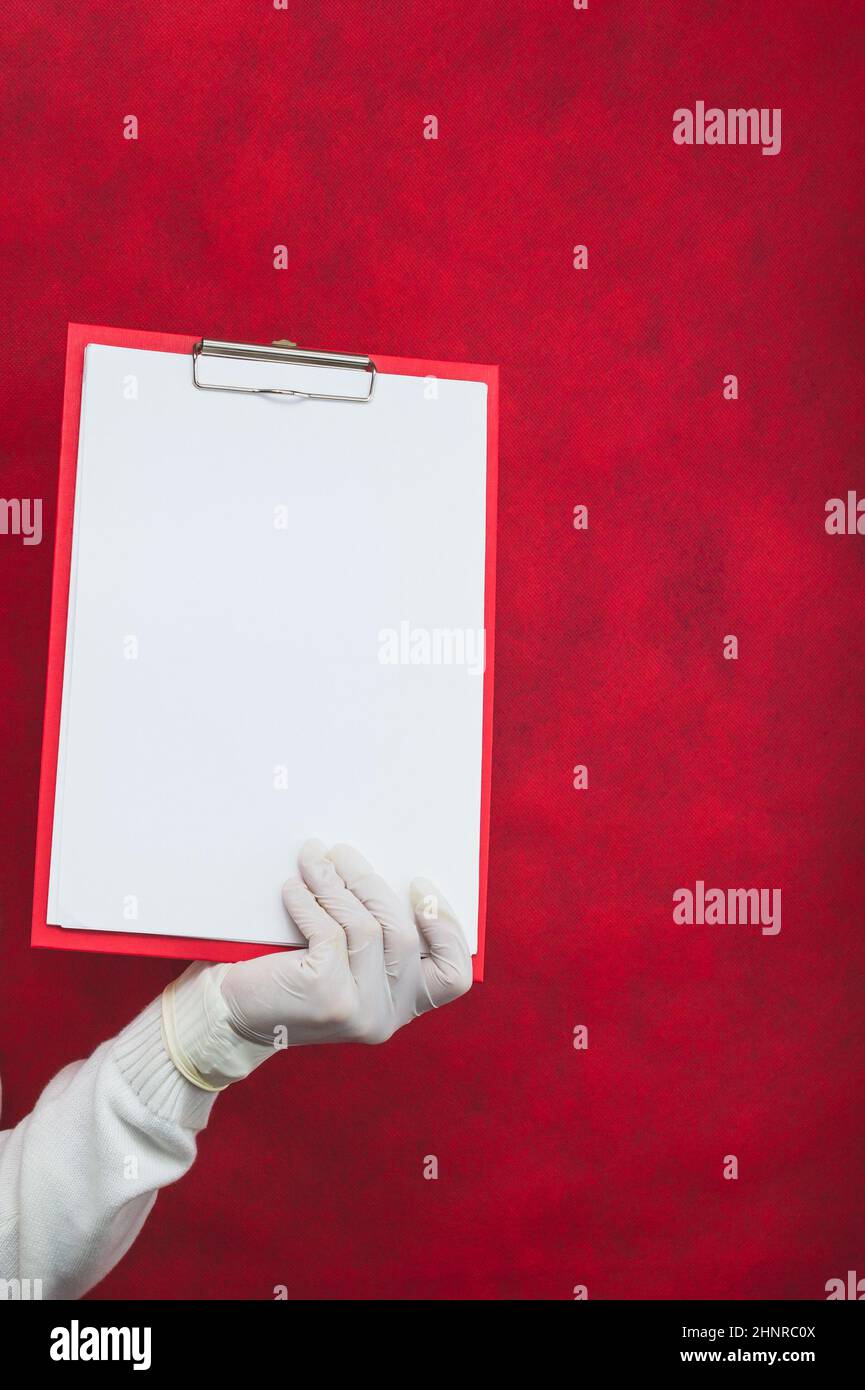 Hand in surgical glove holding white blank paper sheet on red ...