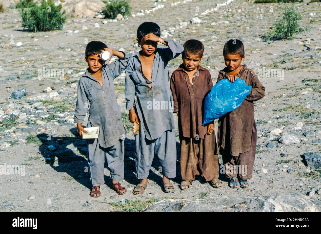 poor children in dirty local clothes pose in the dusty grey mountain landscape at the Karacorum highway Stock Photo