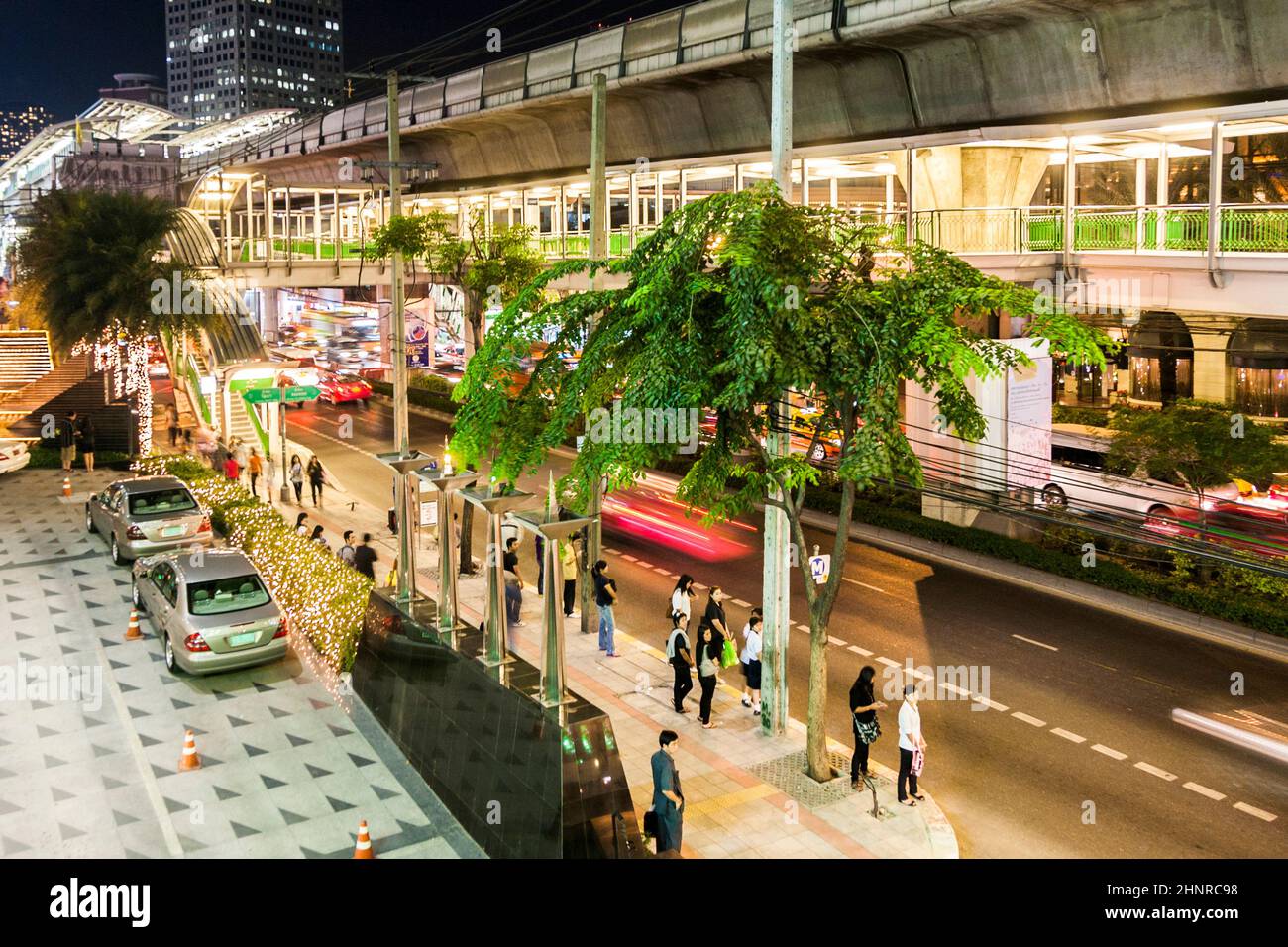 Main road Sukhumvit with people and traffic in Bangkok by night with sky train station Stock Photo