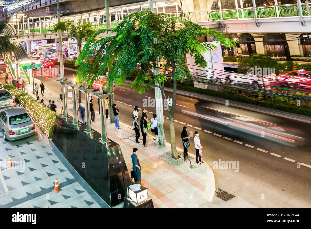 Main road Sukhumvit with people and traffic in Bangkok by night with sky train station Stock Photo