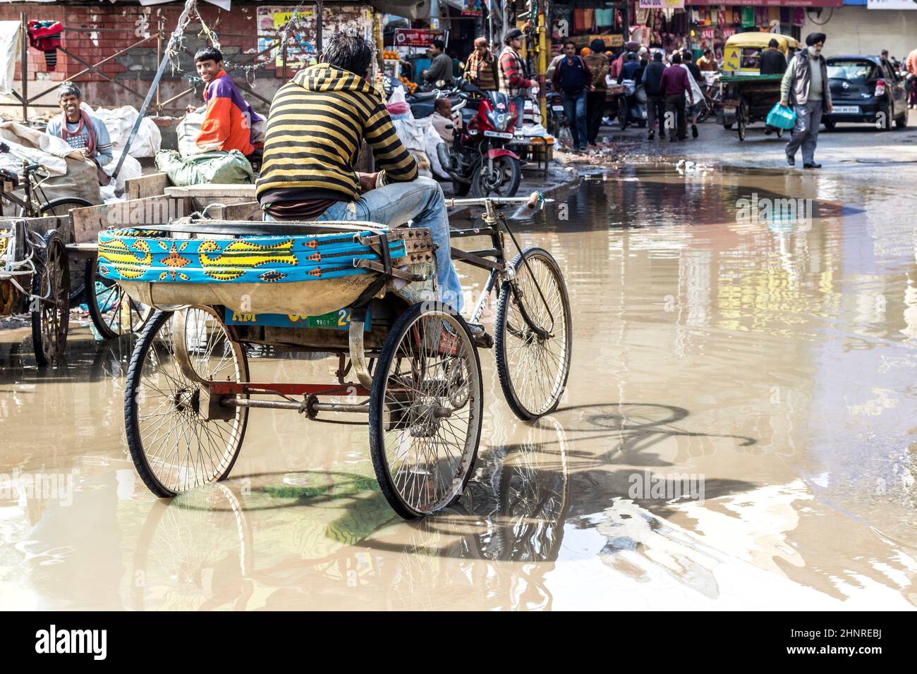 young rickshaw driver waits for guests at the flooded street in rainy season Stock Photo