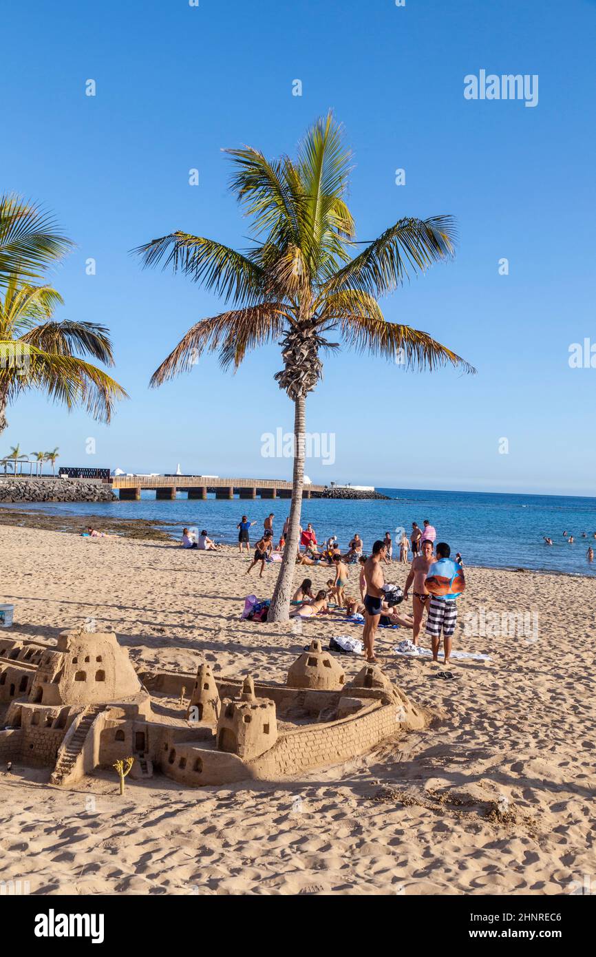 people enjoy the beach in Arrecife and builf castles with sand under palms Stock Photo