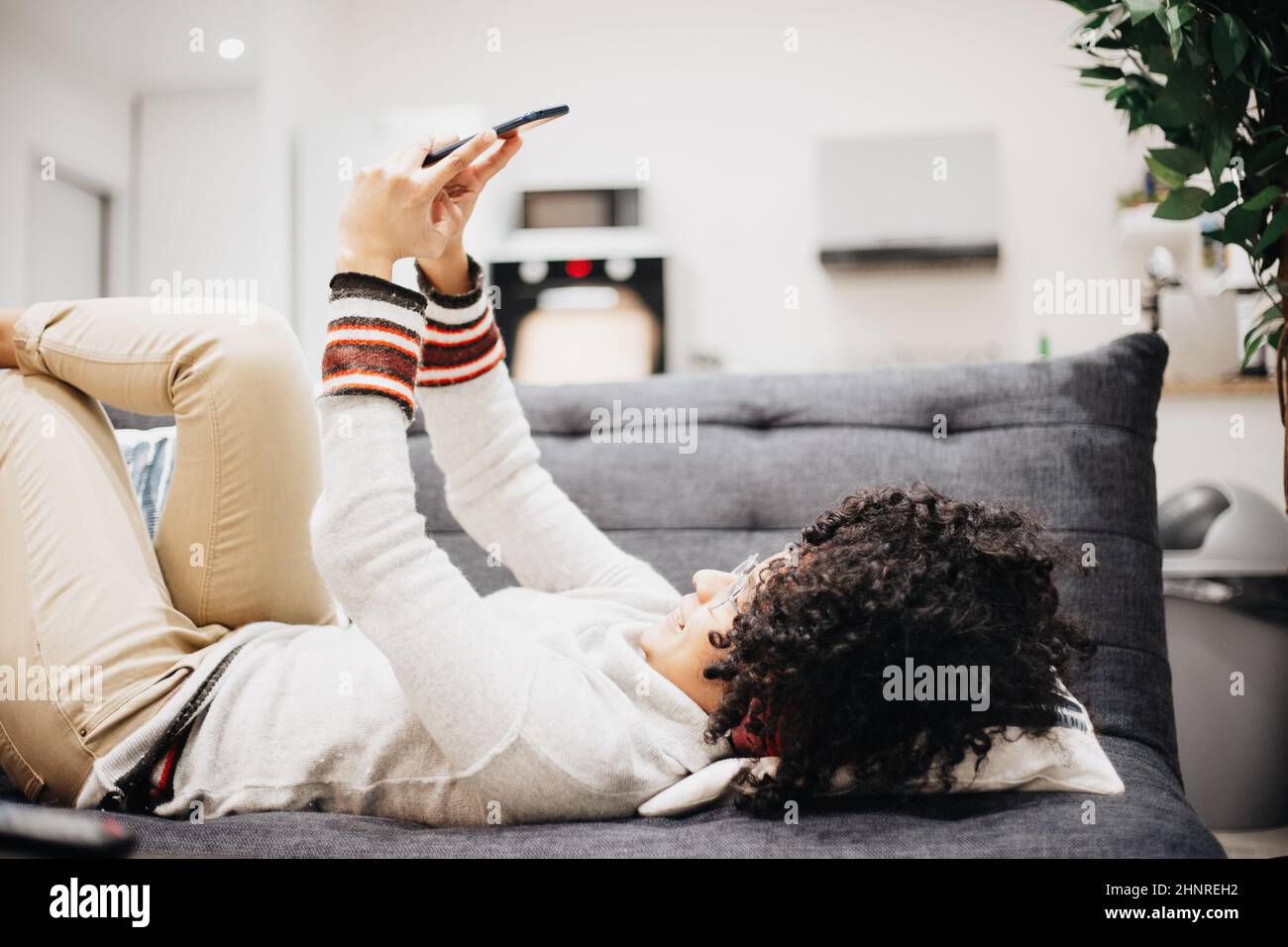 young afro looking at his cell phone lying on sofa of his house Stock Photo