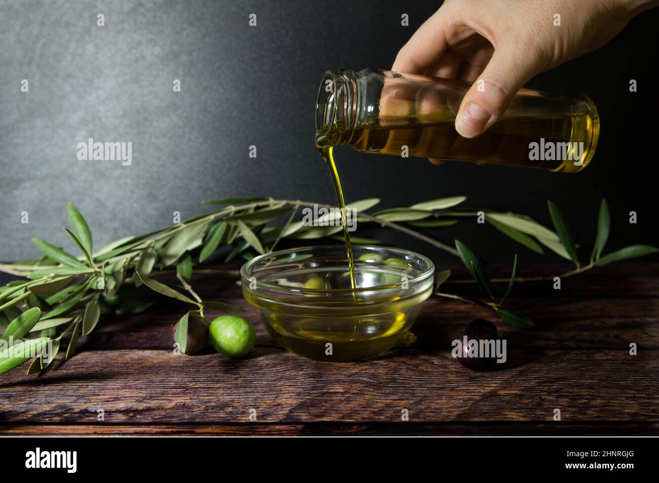Hand pouring olive oil on wooden table Stock Photo