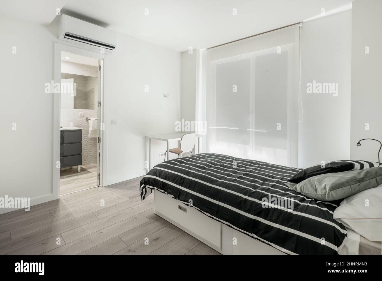 Bedroom with single bed with white wooden furniture, wooden floor and en-suite bathroom in a vacation rental apartment Stock Photo