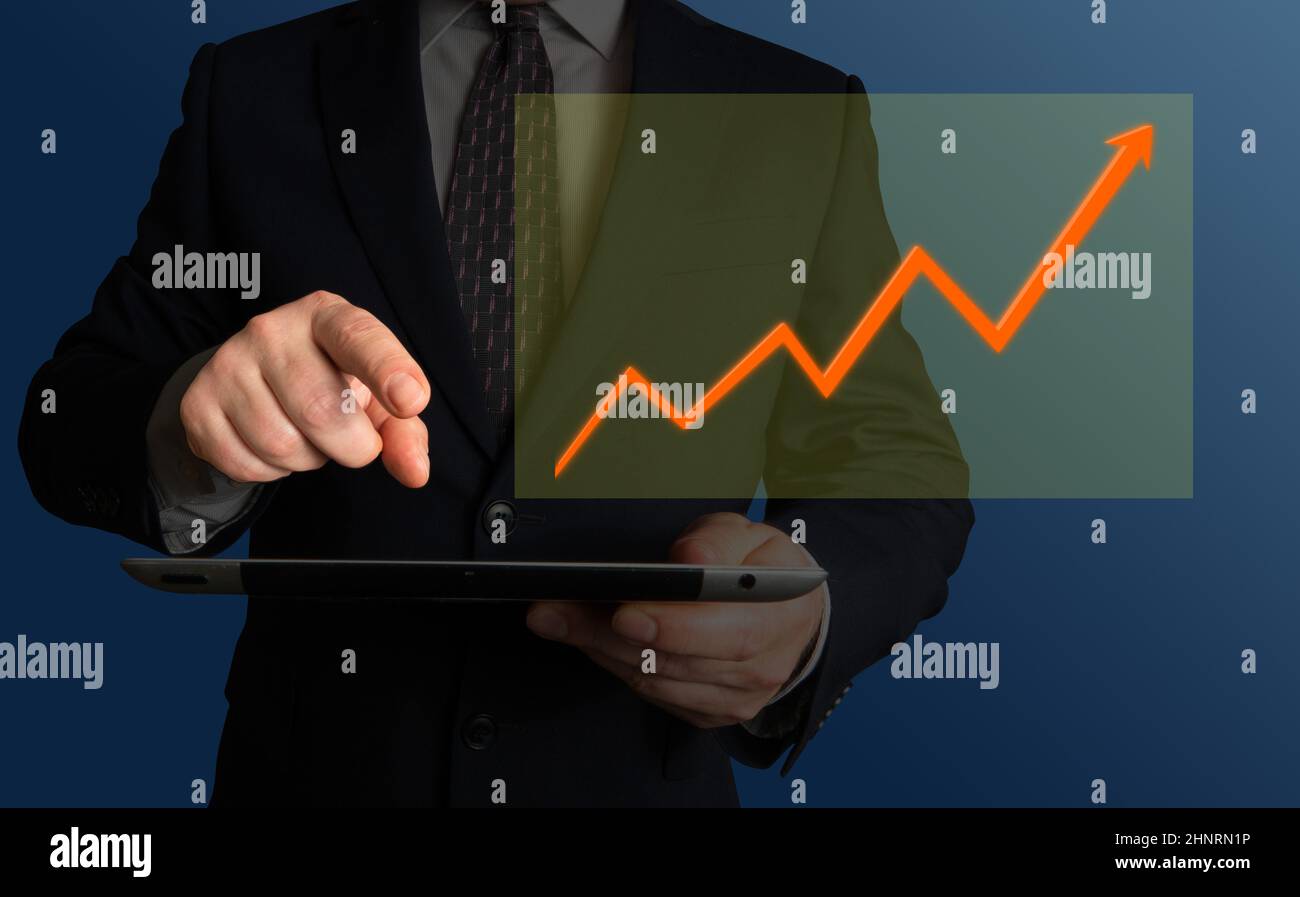 Increasing revenues, profit, quality or satisfaction rates. Businessman holding a tablet or a phone looking at a screen displaying a chart. Stock Photo