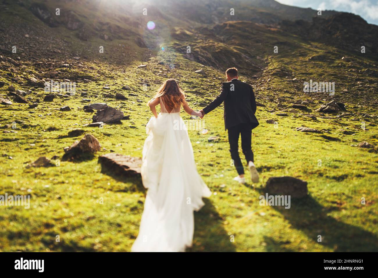 Back view of loving newlyweds, bride in wedding dress running to the