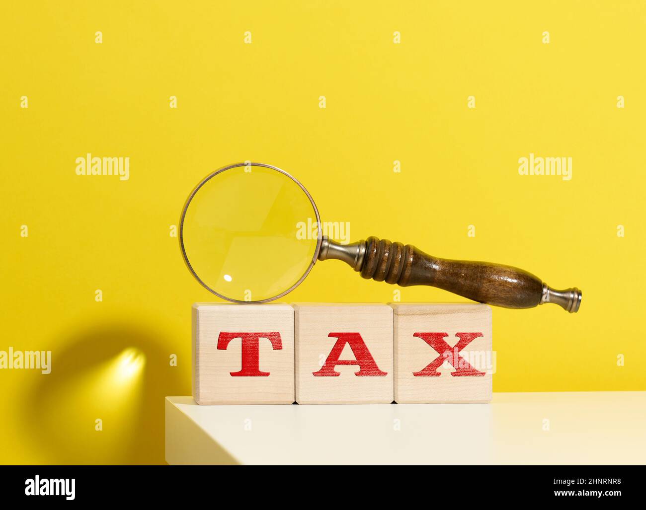 wooden cubes with the inscription tax and a brown magnifying glass on a yellow background Stock Photo