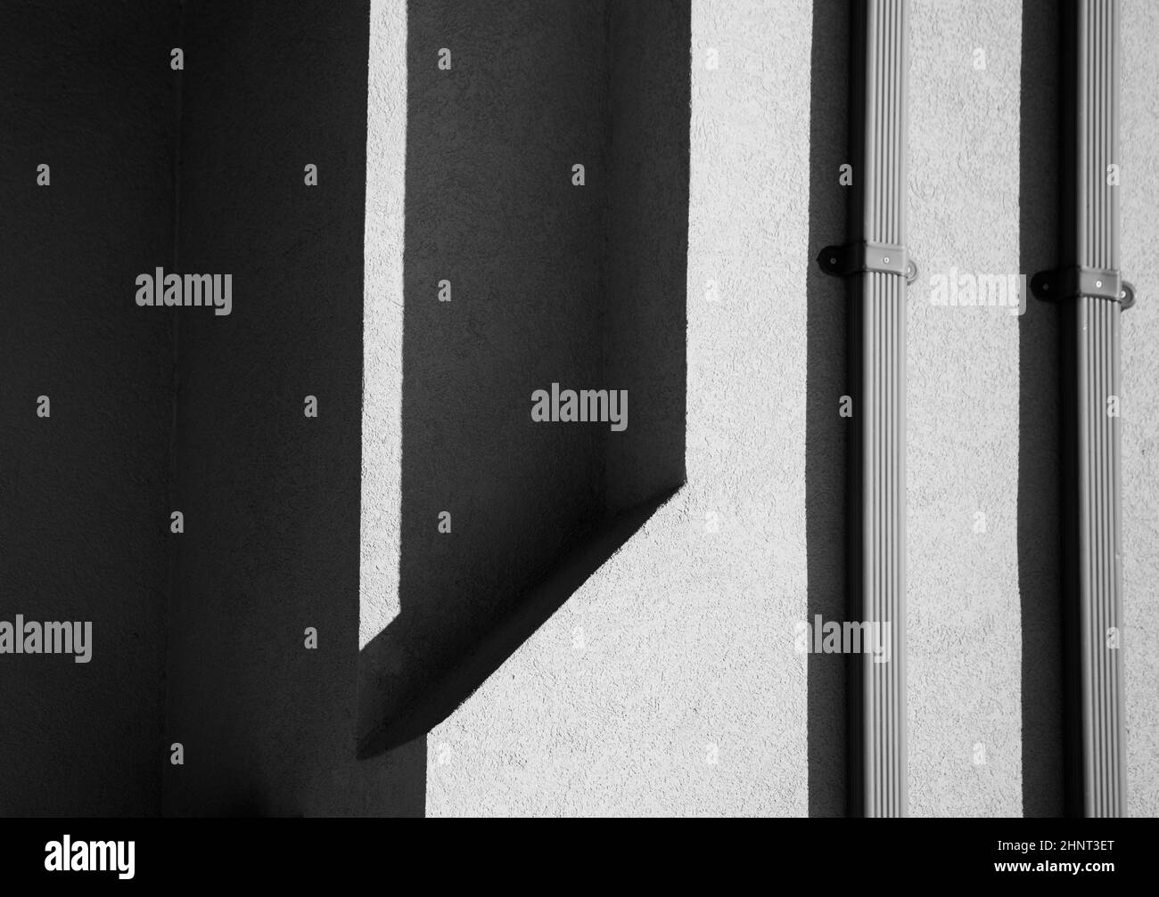 black and white shapes and patterns from shadows cast onto cement concrete wall by afternoon sunlight building exterior two silver metal downspouts Stock Photo