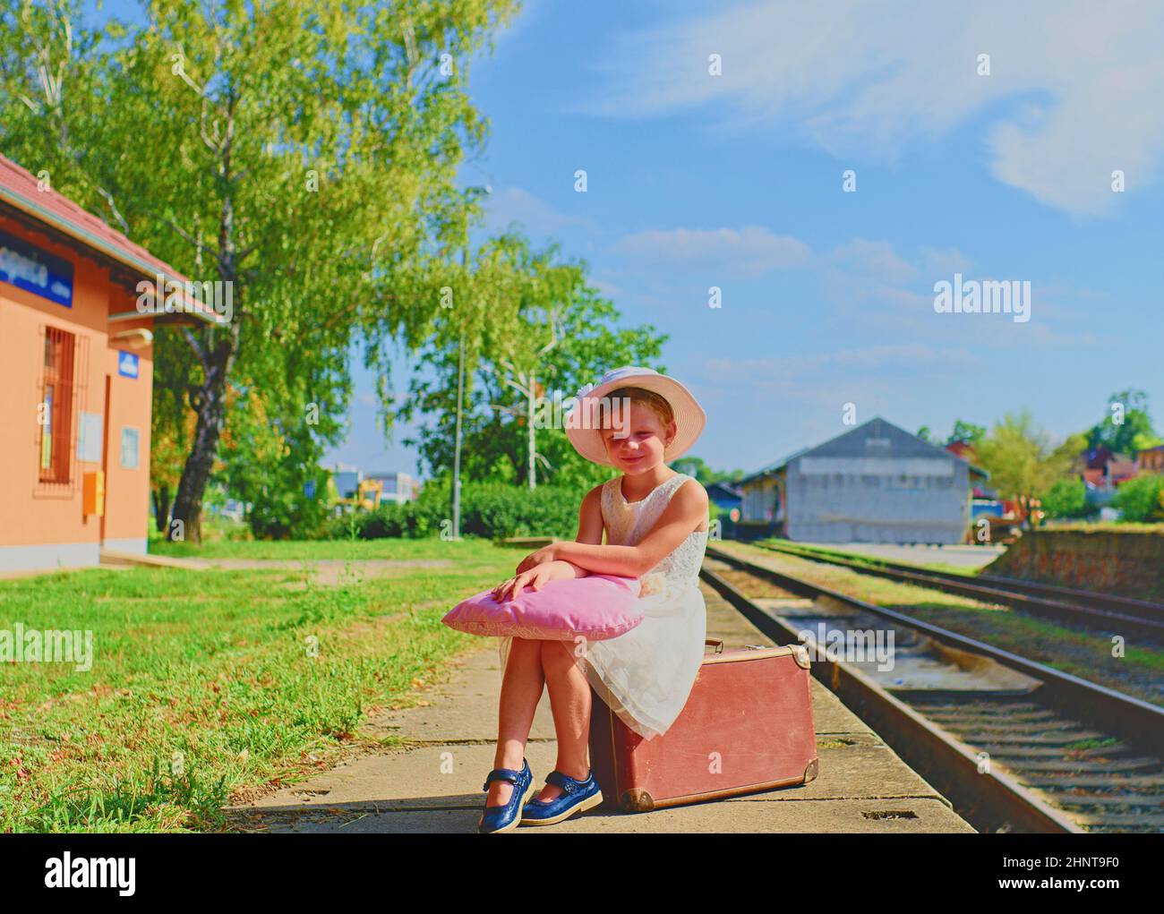 Adorable little girl on a railway station, waiting for the train with vintage suitcase. Traveling, holiday and chilhood concept. Travel insurance concept Stock Photo
