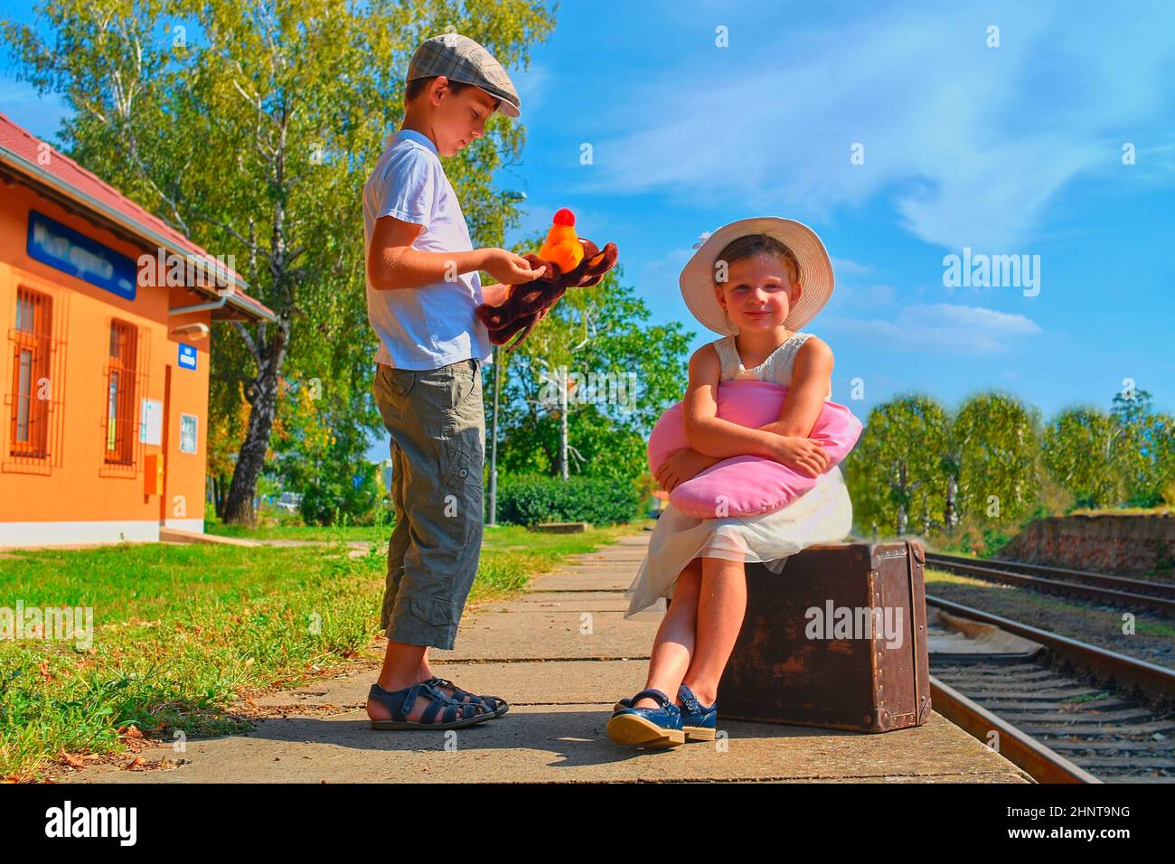 Little children - girl and boy on a railway station, waiting for the train with vintage suitcase. Traveling, holiday and chilhood concept. Travel insurance concept. Travel, tourism, summer vacation and family concept Stock Photo