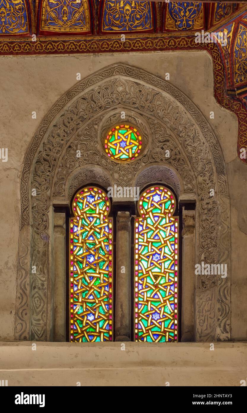 Two adjacent perforated stucco arched windows with colorful stain glass patterns, at Qalawun complex, Cairo, Egypt Stock Photo