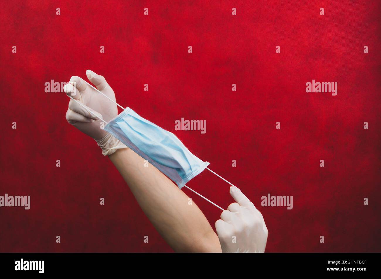 Hands in protective gloves stretch a medical mask on a red background