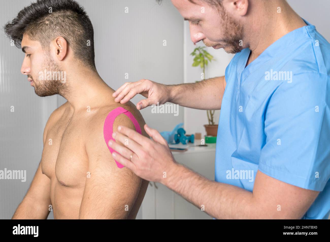 Physical therapist applying kinesio tape on male patient shoulder. Kinesiology, physical therapy, rehabilitation concept. close up Stock Photo