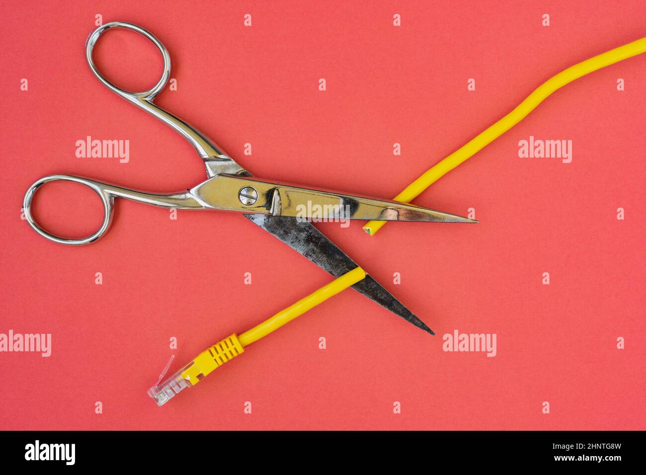 Scissors cutting the yellow network cable. Prohibit and restrict access to the internet, limit internet connection concepts. Stock Photo