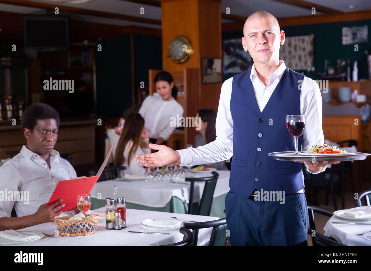 Hospitable waiter guests in cozy restaurant hall Stock Photo