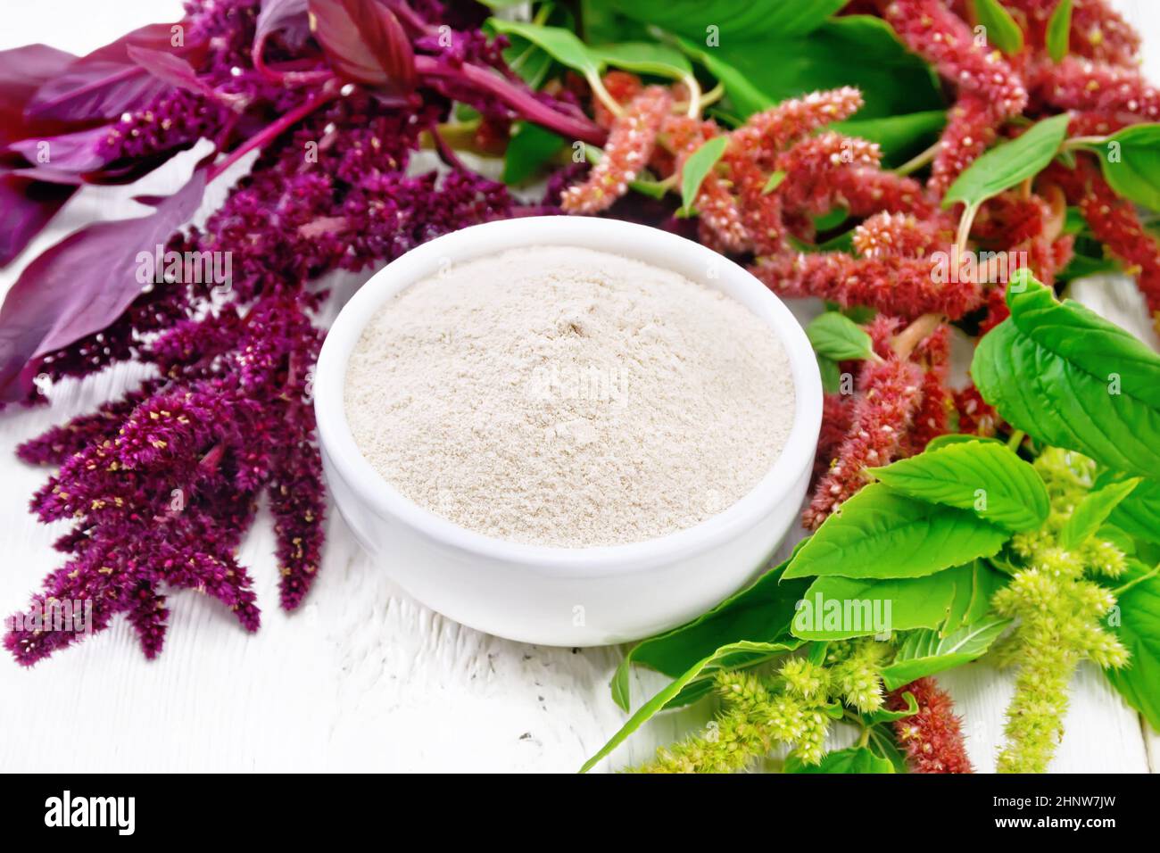 Amaranth flour in a bowl, brown, green and purple flowers and leaves of a plant on the background of light wooden board Stock Photo