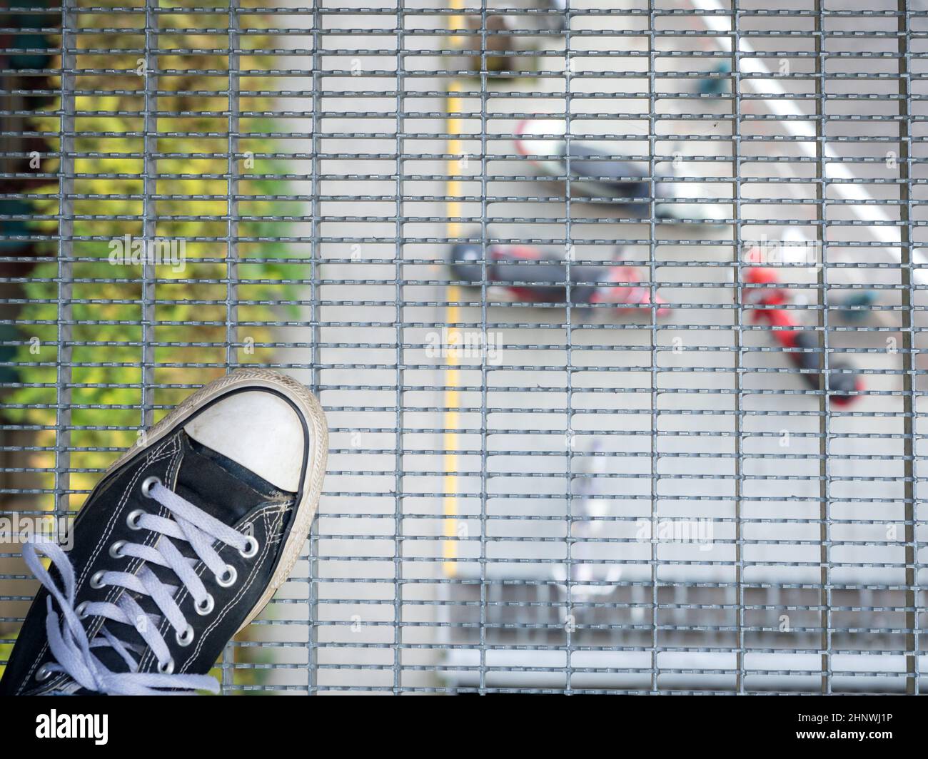 Posing in great height looking through a steel mesh down to a street