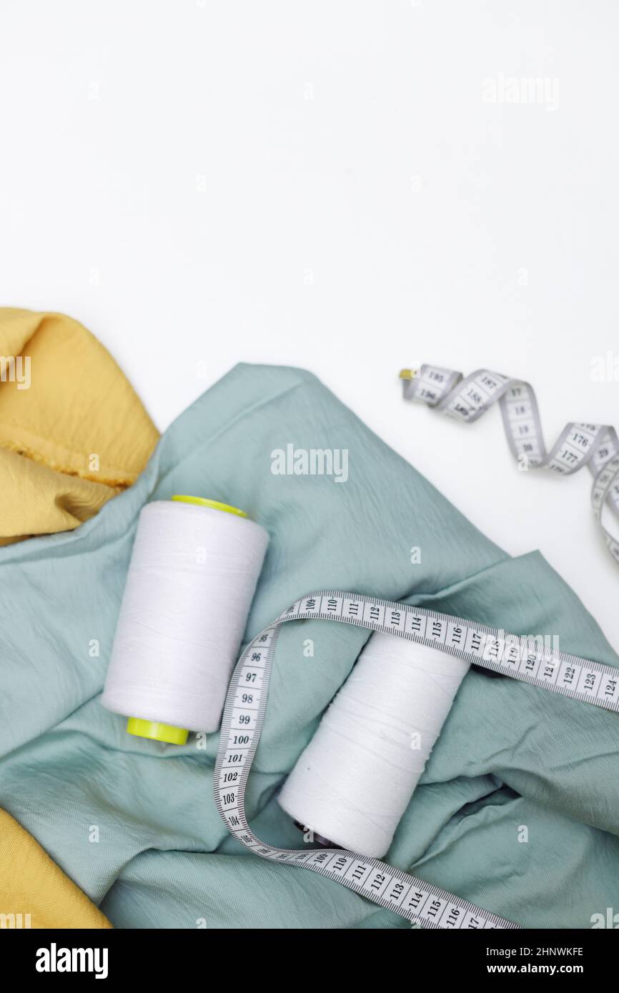 Various fabrics, measuring tape and thread isolated on white. Flat lay
