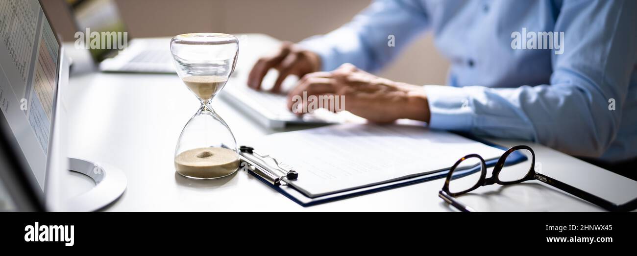 Late Invoice And Billing Deadline With Hourglass At Desk Stock Photo