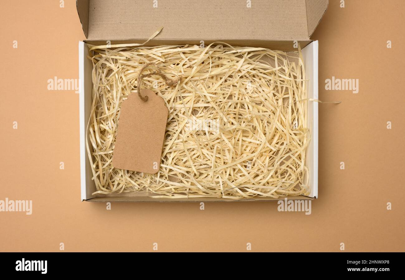 empty rectangular open corrugated paper box with sawdust inside. Packaging, containers for transportation on a brown background Stock Photo