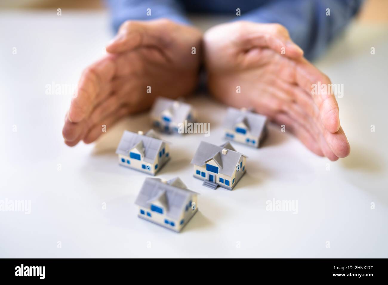Hand Protecting Miniature Houses On The Desk Stock Photo