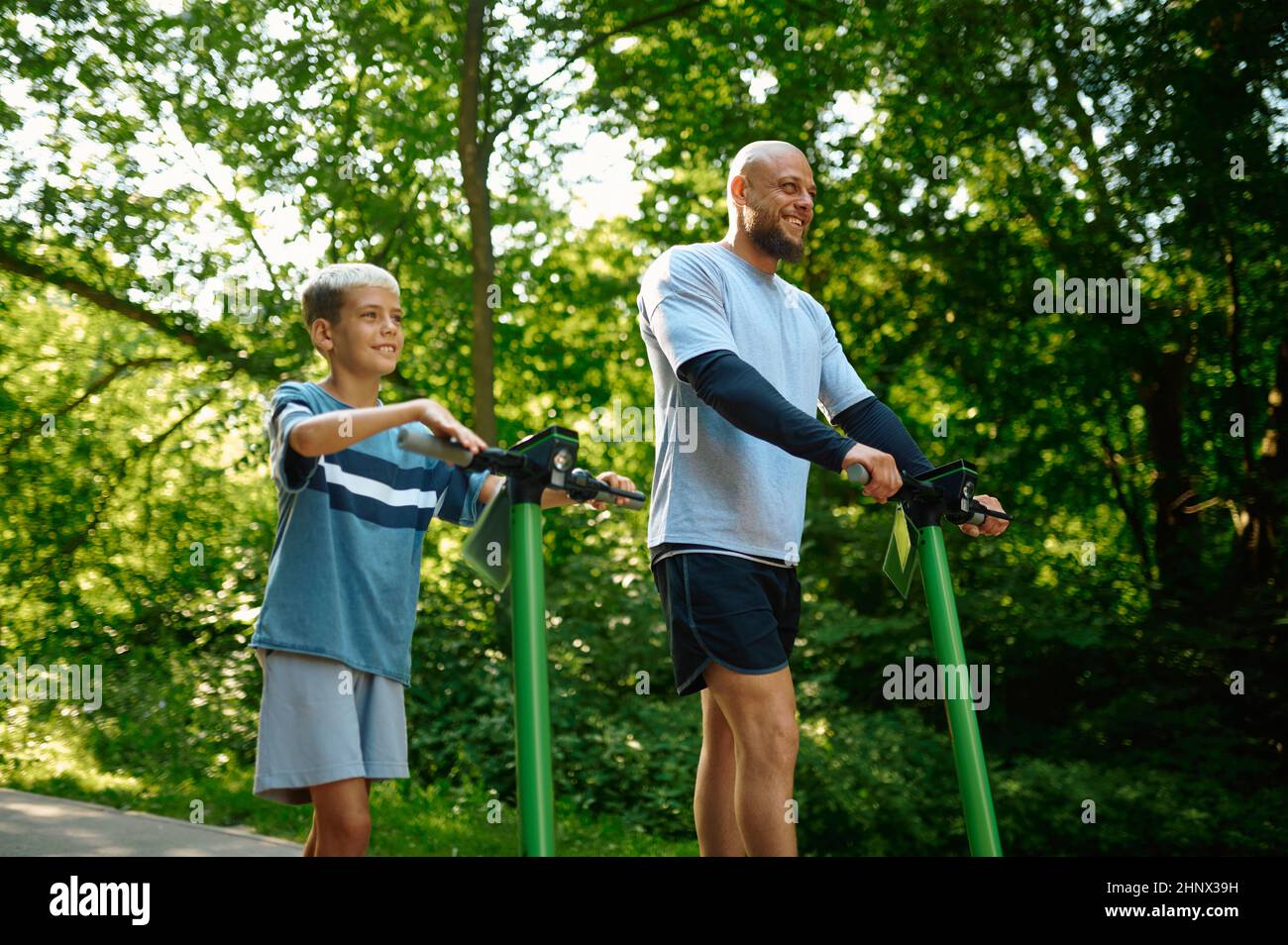 Father and boy riding on kick scooters in summer park. The family leads