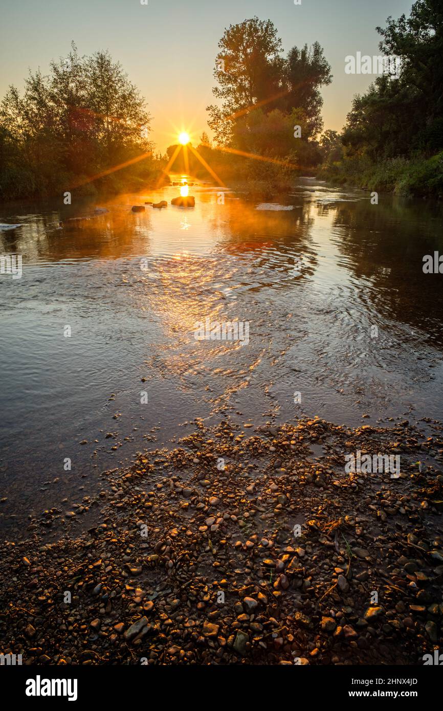 Sunrise sunstar sunbeams river landscape vertical format Stock Photo