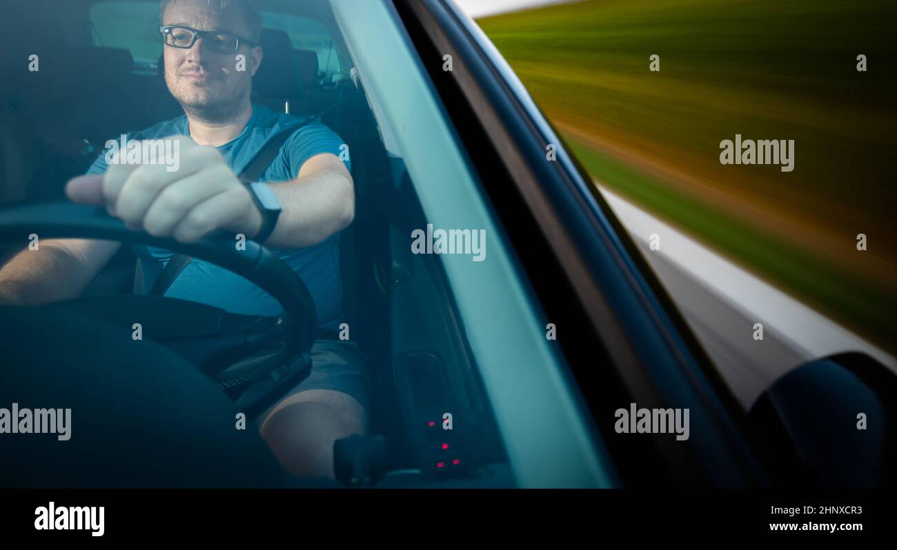 Handsome young driver driving hic car fast yet safely on the road (motion blurred image) Stock Photo