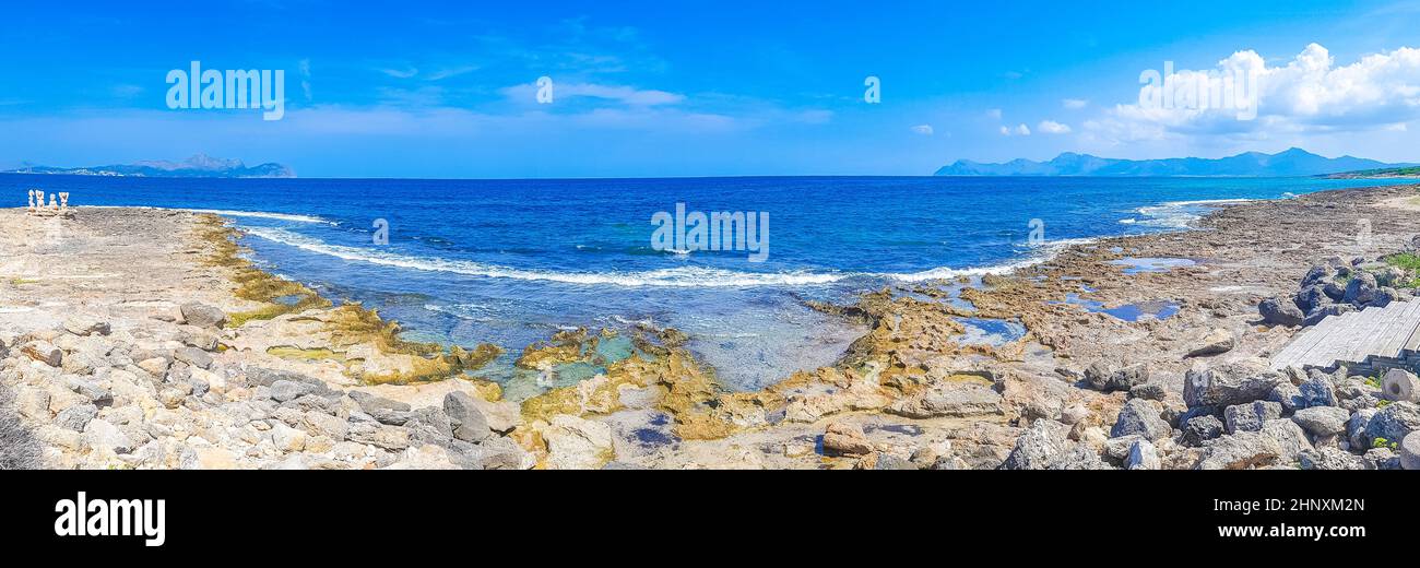 Rough natural coastal and beach landscape panorama with turquoise water waves mountains rocks boulders and stone sculptures in Can Picafort on Baleari Stock Photo
