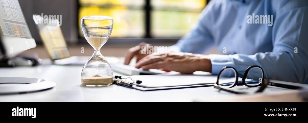 Late Invoice And Billing Deadline With Hourglass At Desk Stock Photo