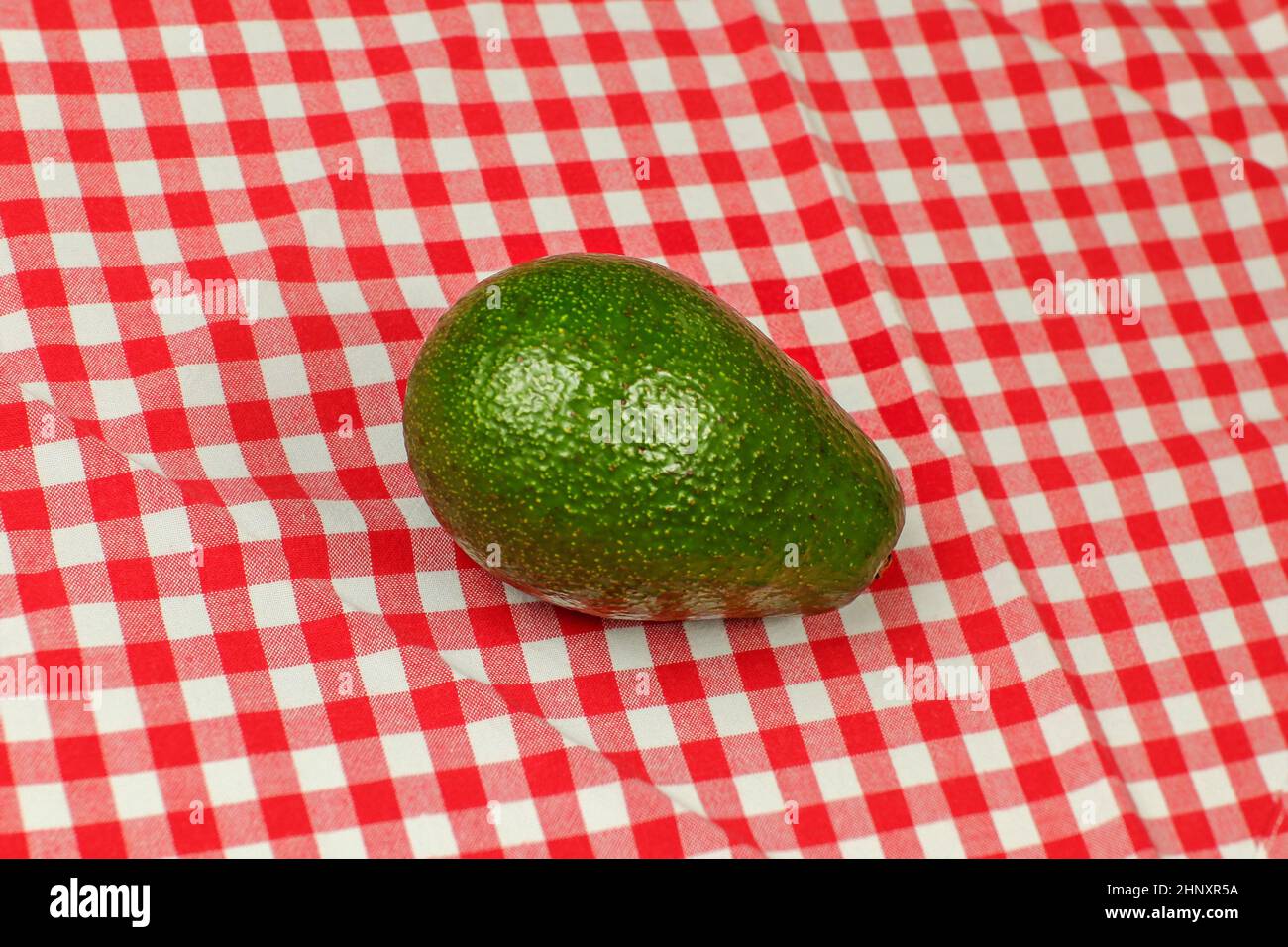 Whole avocado on red checkered tablecloth Stock Photo