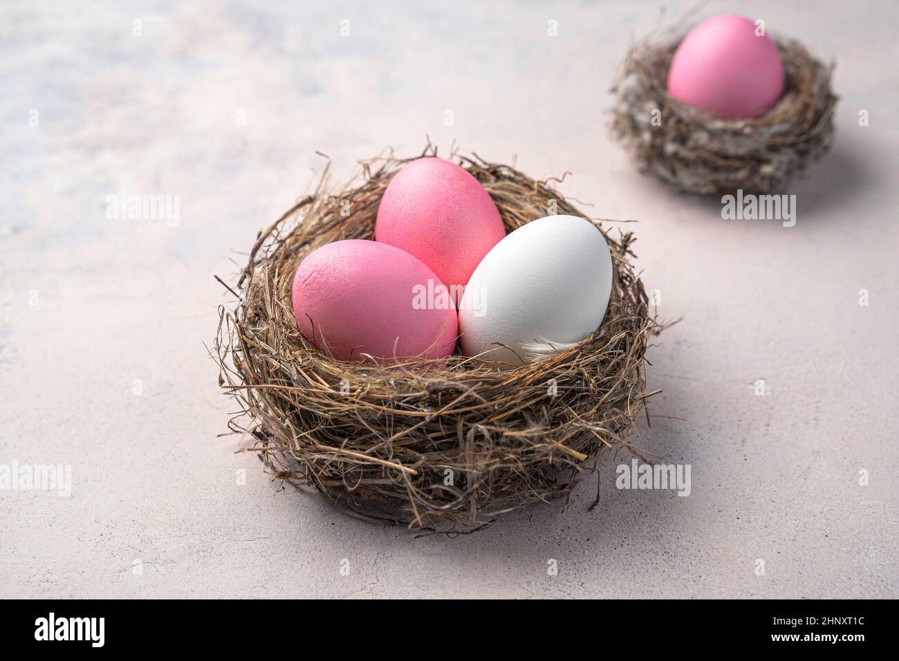 Three Easter eggs in a nest on a light background. Easter background. Side view, close-up. Stock Photo