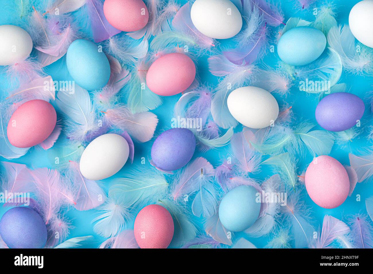 Colored Easter eggs and feathers on a blue background. Top view. Easter background. Stock Photo