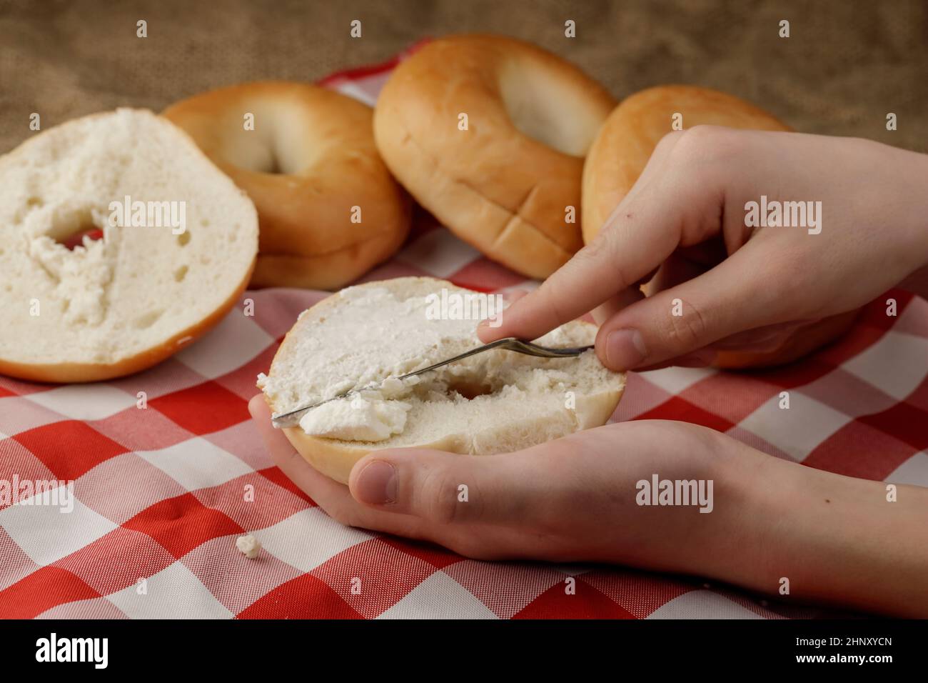 A studio photo of spreading cream cheese on an open plain bagel Stock