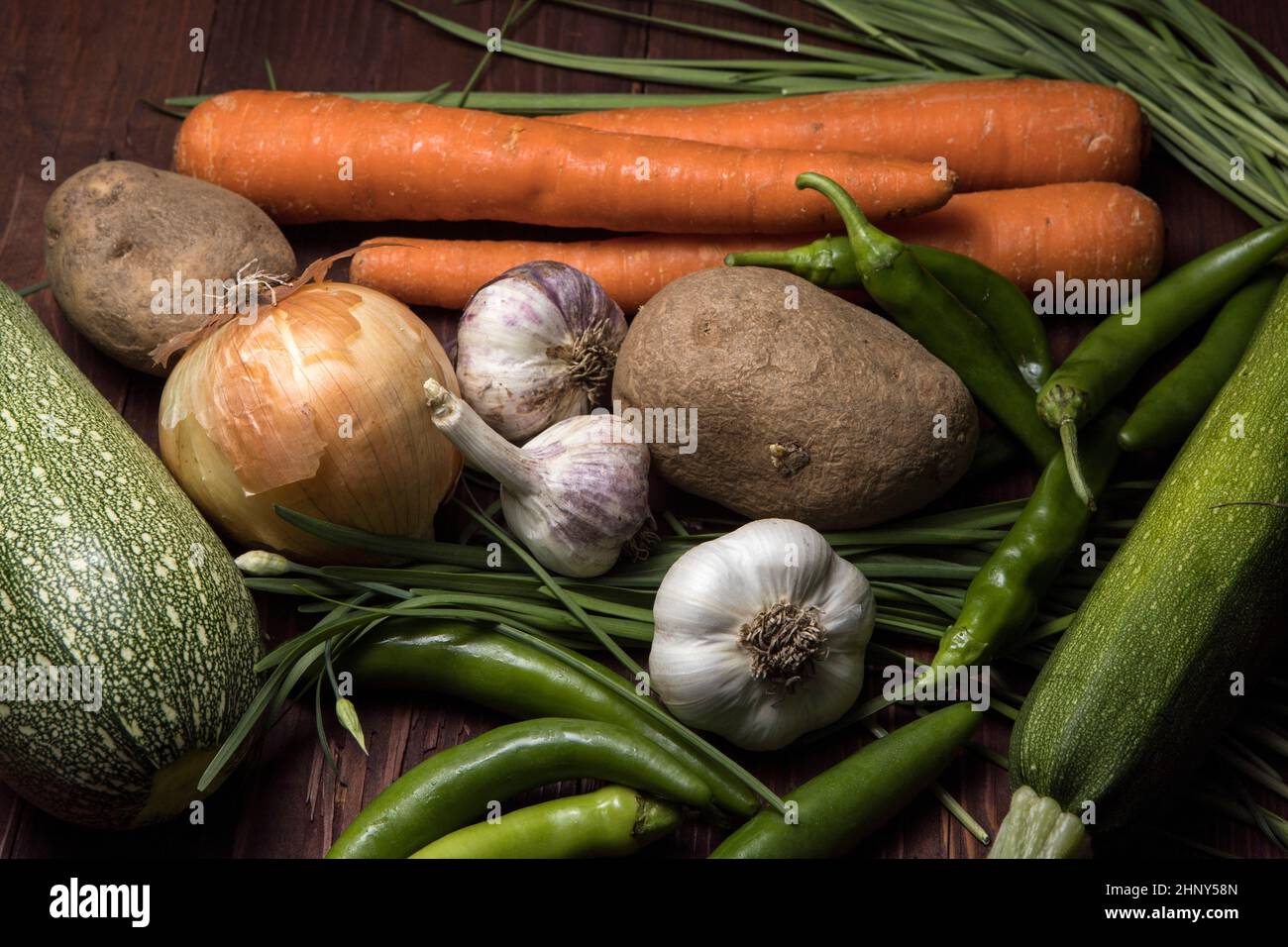 A close up of a bunch of assorted vegetables such as garlic, carrots, chives, onions, potatoes, and peppers. Stock Photo
