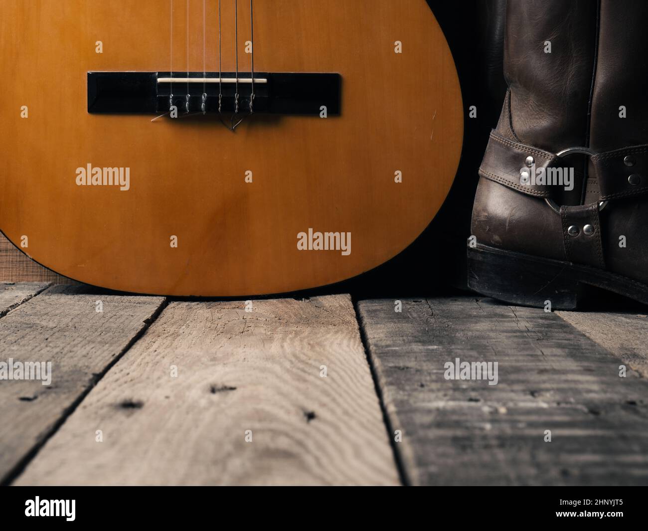 Old cowboy boots with an acoustic guitar on barn wood, space for your text Stock Photo