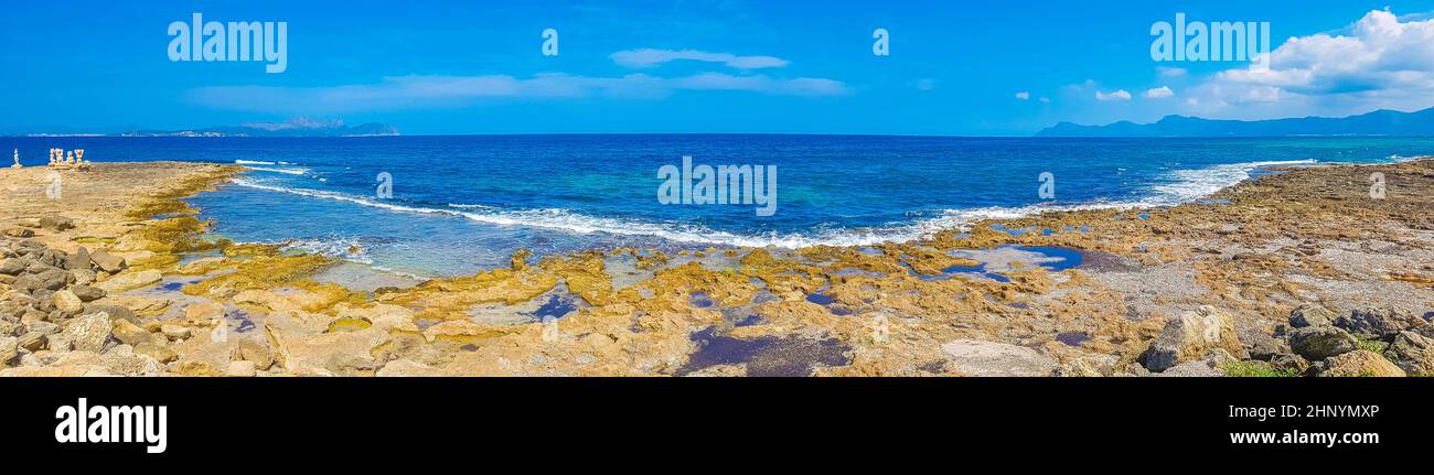 Rough natural coastal and beach landscape panorama with turquoise water waves mountains rocks boulders and stone sculptures in Can Picafort on Baleari Stock Photo