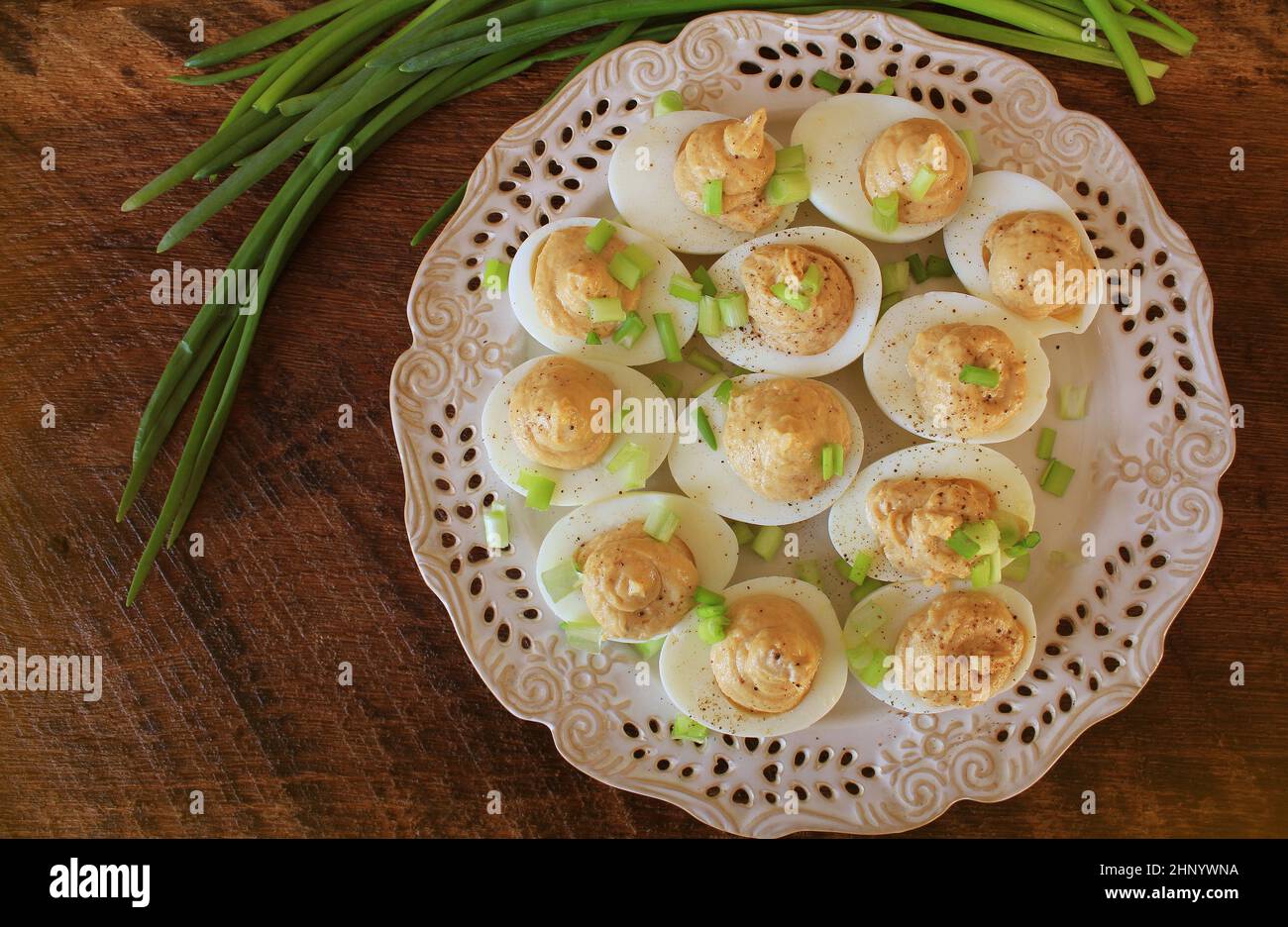 Deviled eggs with cod livers with leek on white plate. Rustic wooden table . Stock Photo