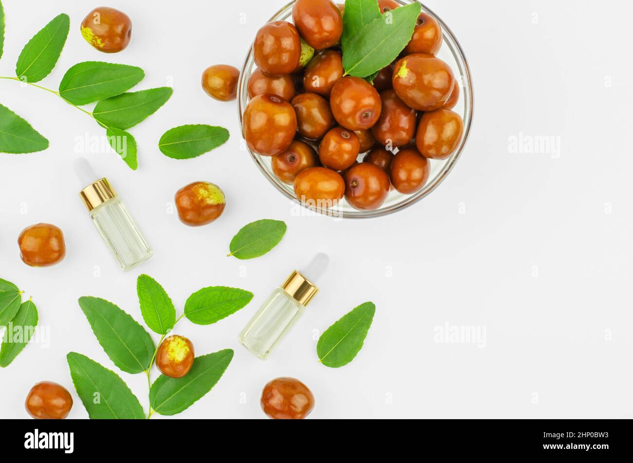 Chinese date oil and fruits, copy space. Jojoba oil in bottles with a dropper on a background with ripe jojoba fruits and green leaves. Stock Photo