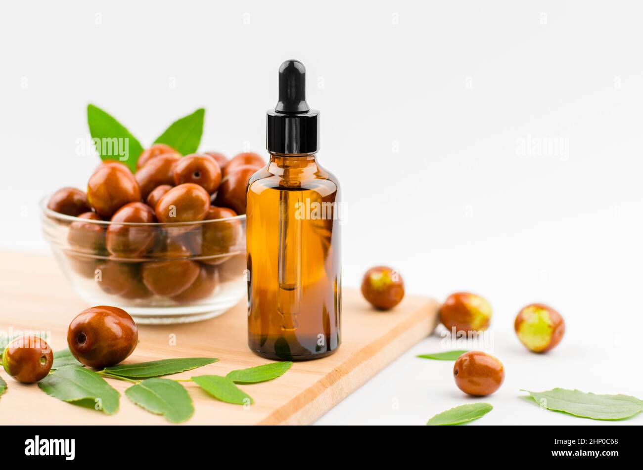 Jojoba oil in a bottle with a dropper on a wooden table with ripe jojoba fruits. Chinese Date Oil and Fruit Stock Photo