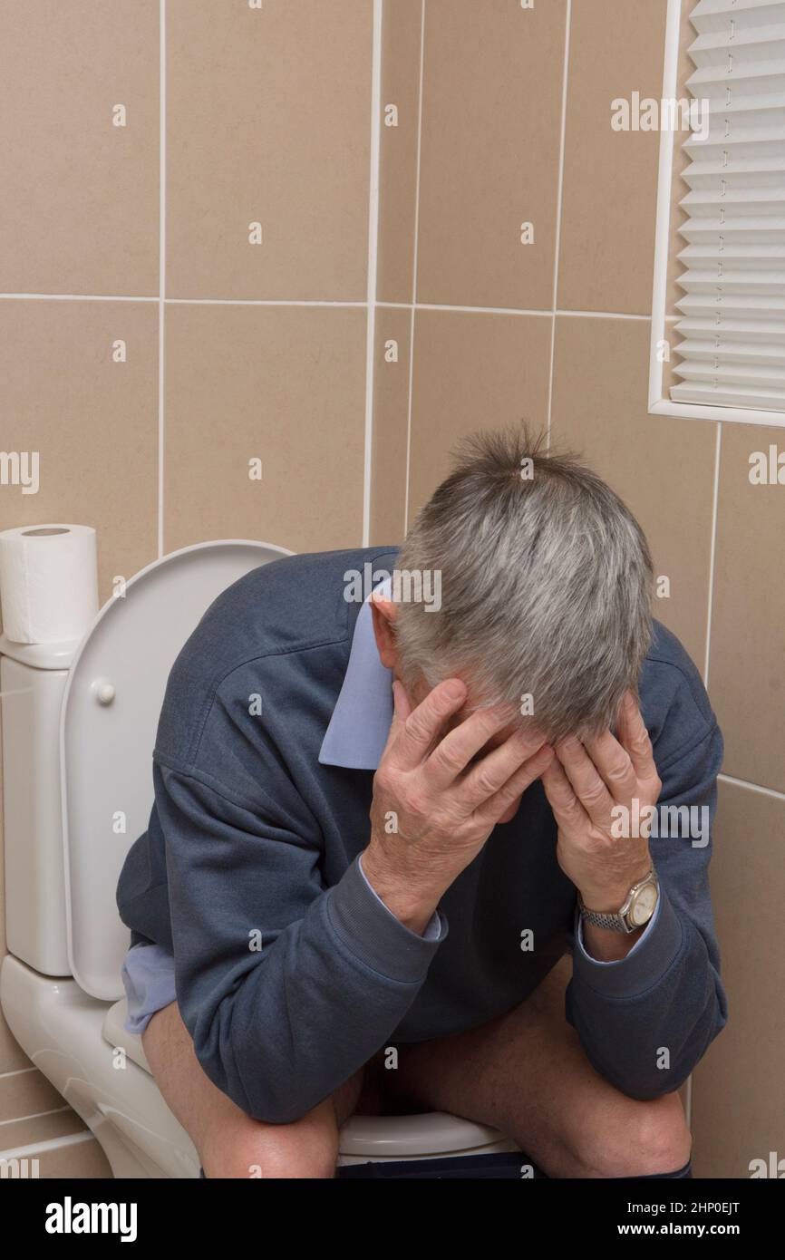 man sitting on toilet holding his head in his hands, diarrhoea or constipation Stock Photo