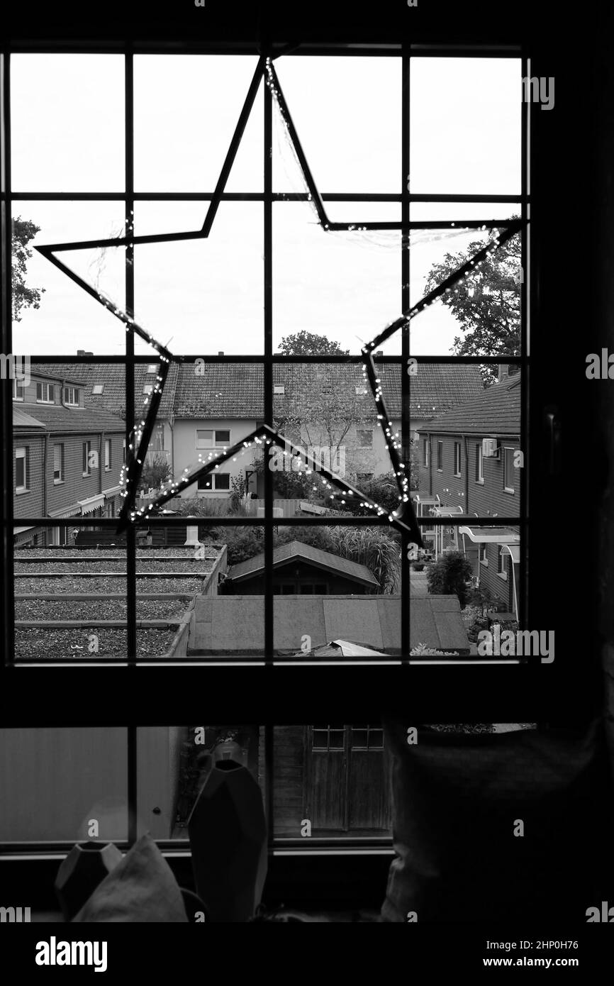Metal star shaped grilles on a window decorated with Christmas lights in black and white Stock Photo