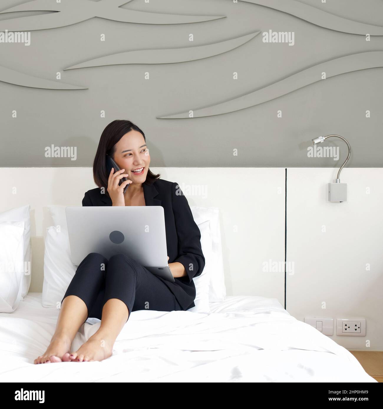 Young asian woman in black suit use laptop computer and mobile phone to ...