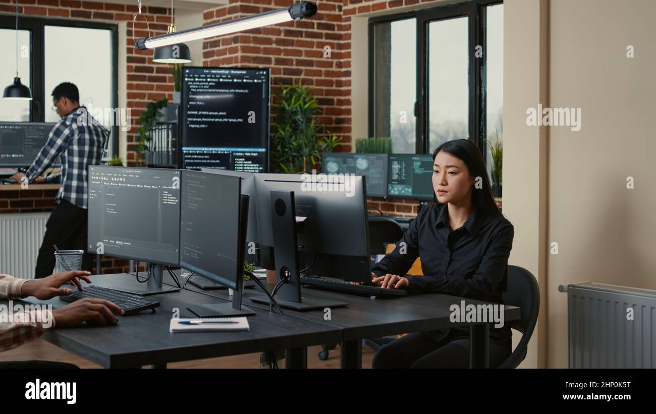 Programer with clipboard sitting down at desk in front of programer writing code while team of database admins compute big data. Team of mixed programmers working on machine learning software. Stock Photo