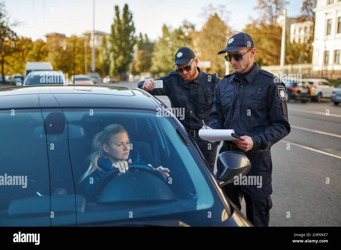 Police patrol checking driver's license of female driver. Policemen in uniform protect the law, registration of an offense. Cops work on city street Stock Photo