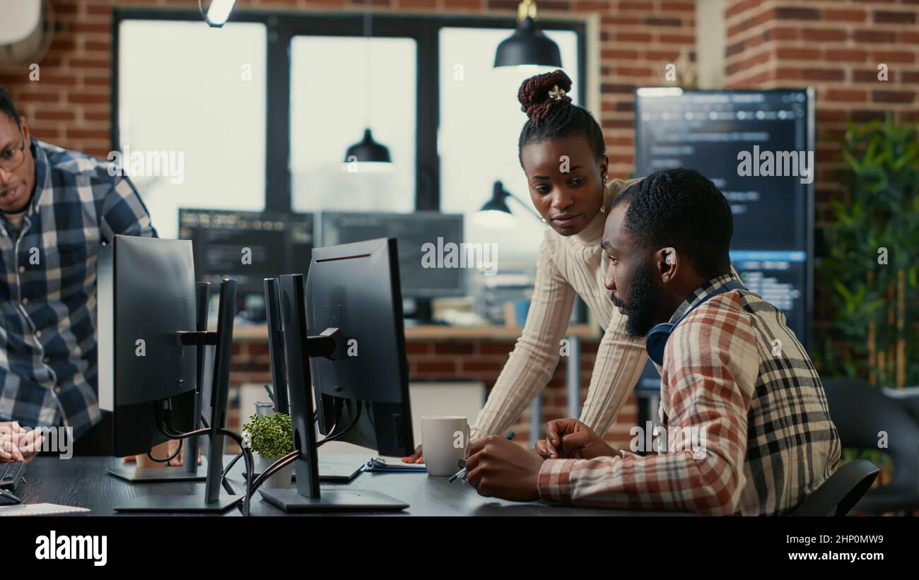 Mixed team of programmers brainstorming ideas for new cloud computing user interface looking at running code on computer screens. Developers collaborating on group project compiling algorithm. Stock Photo