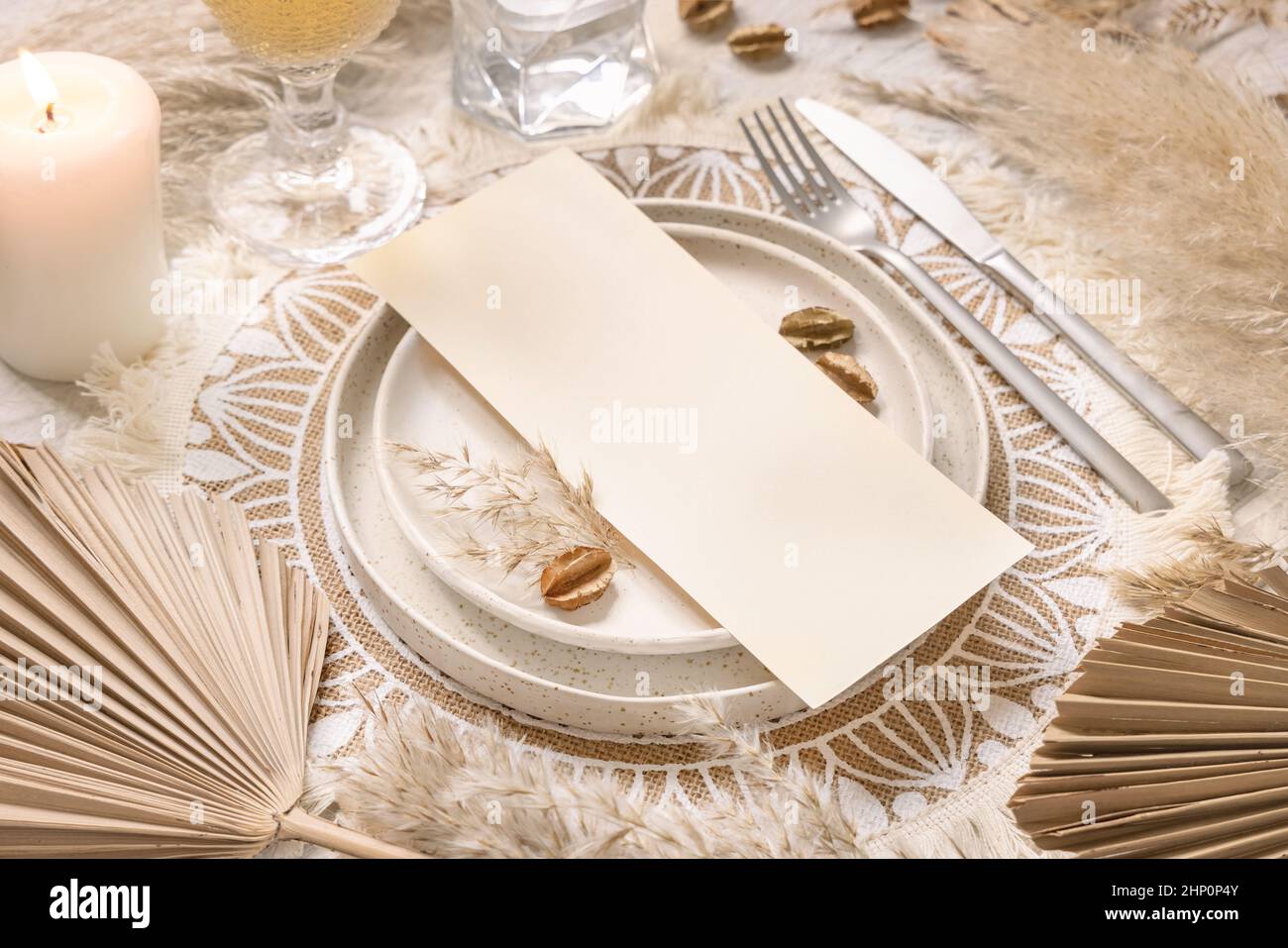 Table place with blank card on white wooden table with bohemian decorations around close up. Boho wedding menu card mockup. Tropical beige template wi Stock Photo