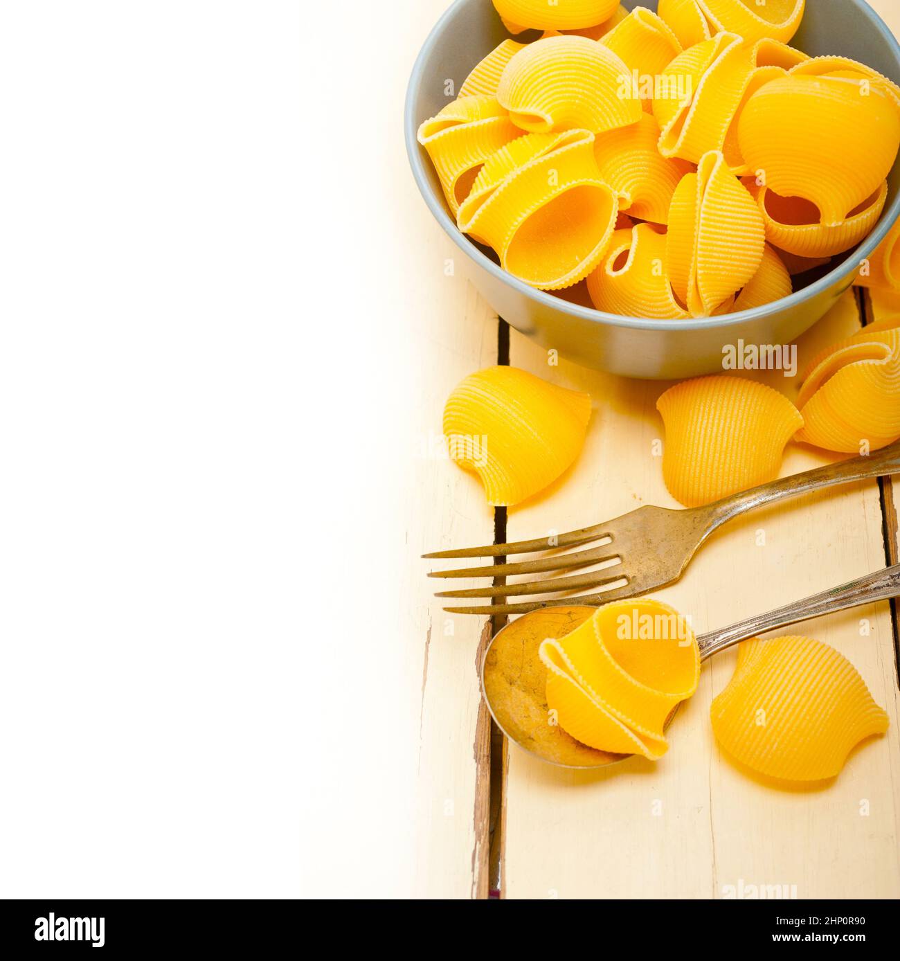 raw Italian snail lumaconi pasta on a blue bowl over rustic table macro ...