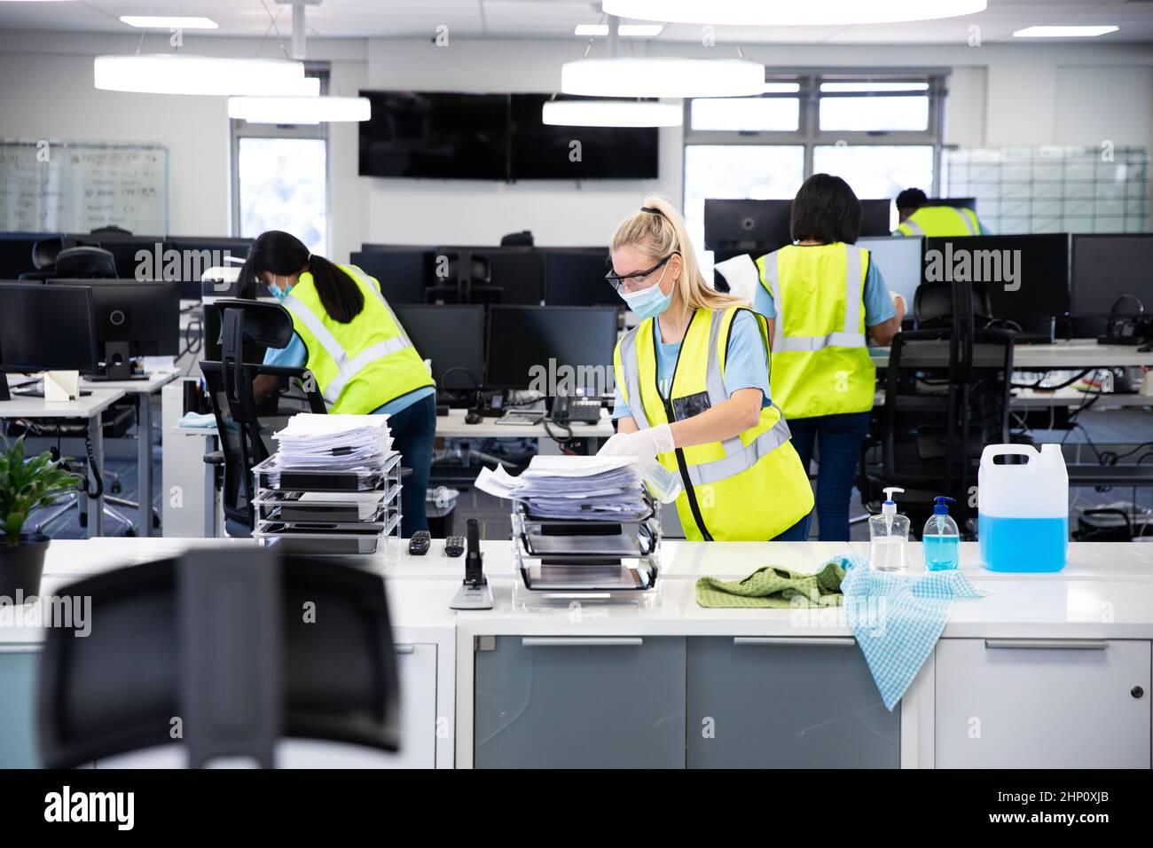 Caucasian woman and colleagues wearing hi vis vests, gloves, safety glasses and face masks sanitizin Stock Photo